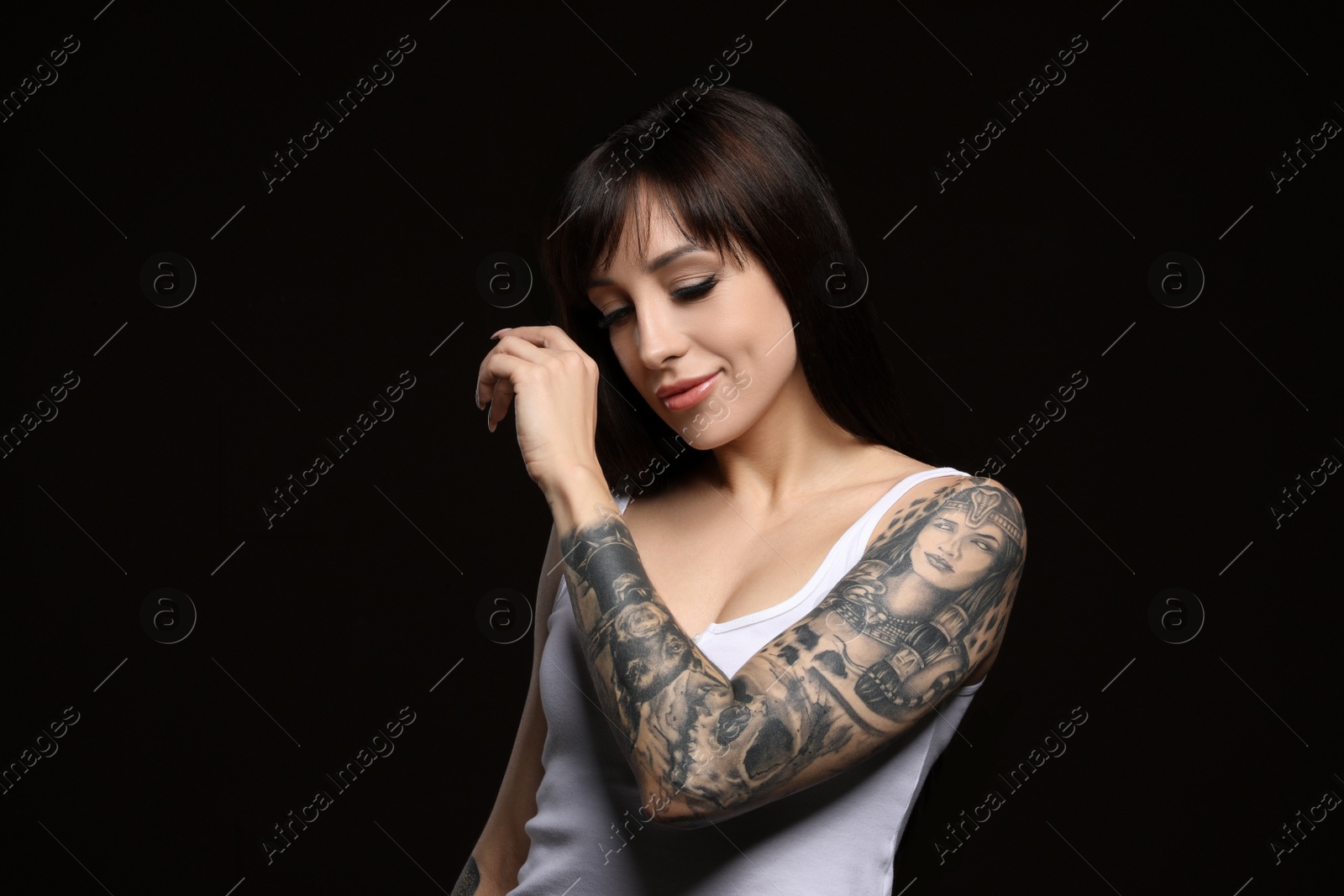 Photo of Beautiful woman with tattoos on arm against black background