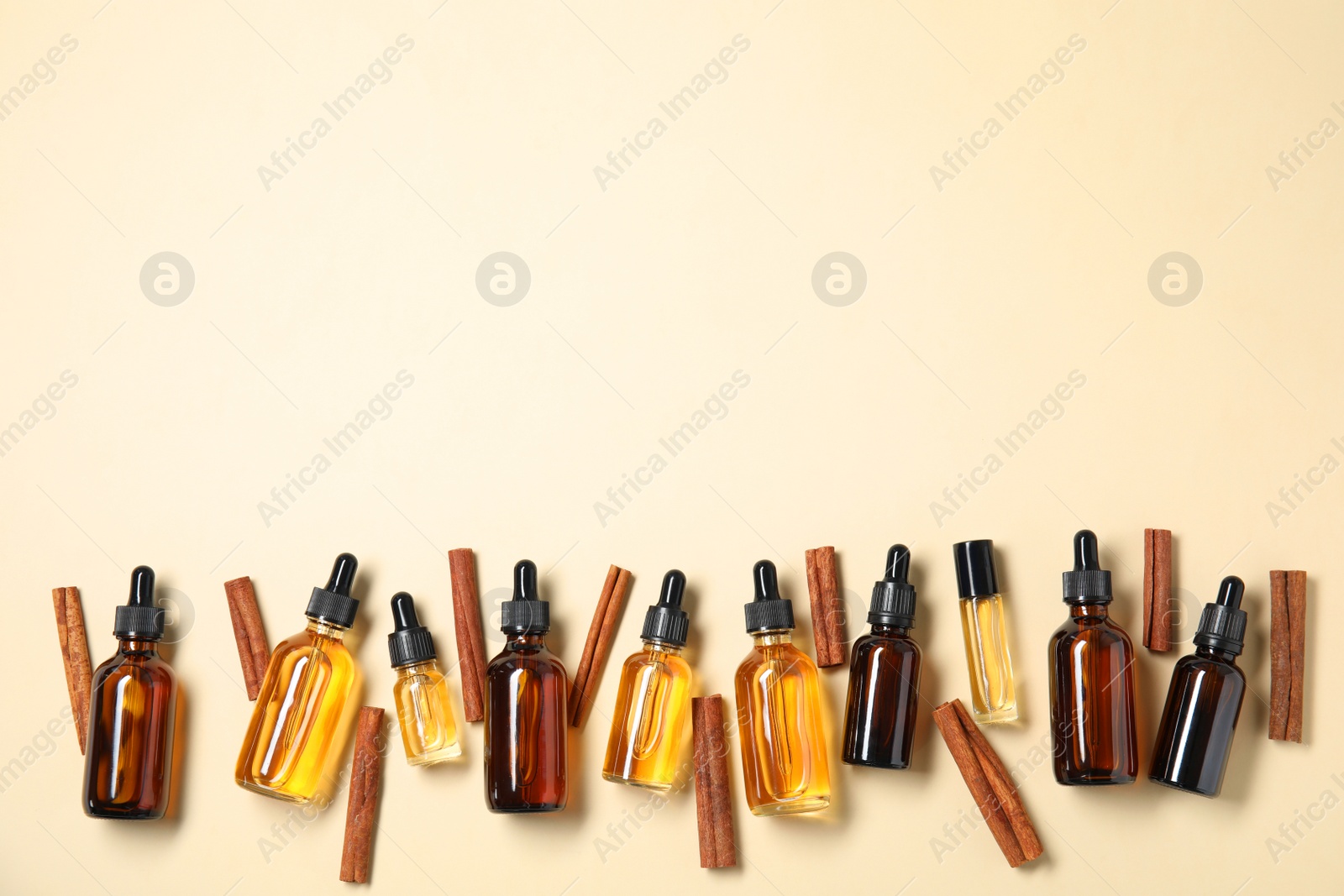 Photo of Flat lay composition with bottles of essential oils and cinnamon sticks on beige background. Space for text