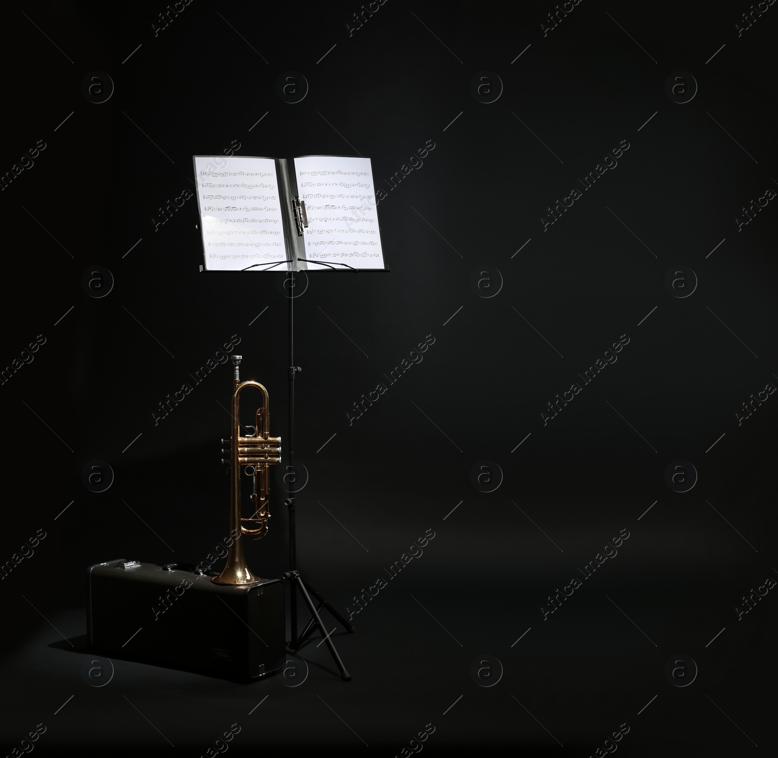 Photo of Trumpet, case and note stand with music sheets on black background. Space for text