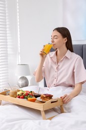 Beautiful woman having tasty breakfast in bed at home