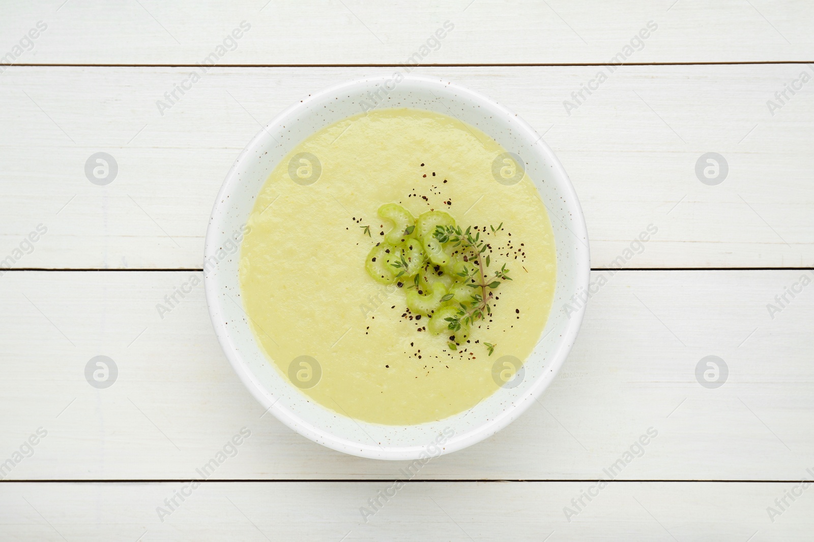 Photo of Bowl of delicious celery soup on white wooden table, top view