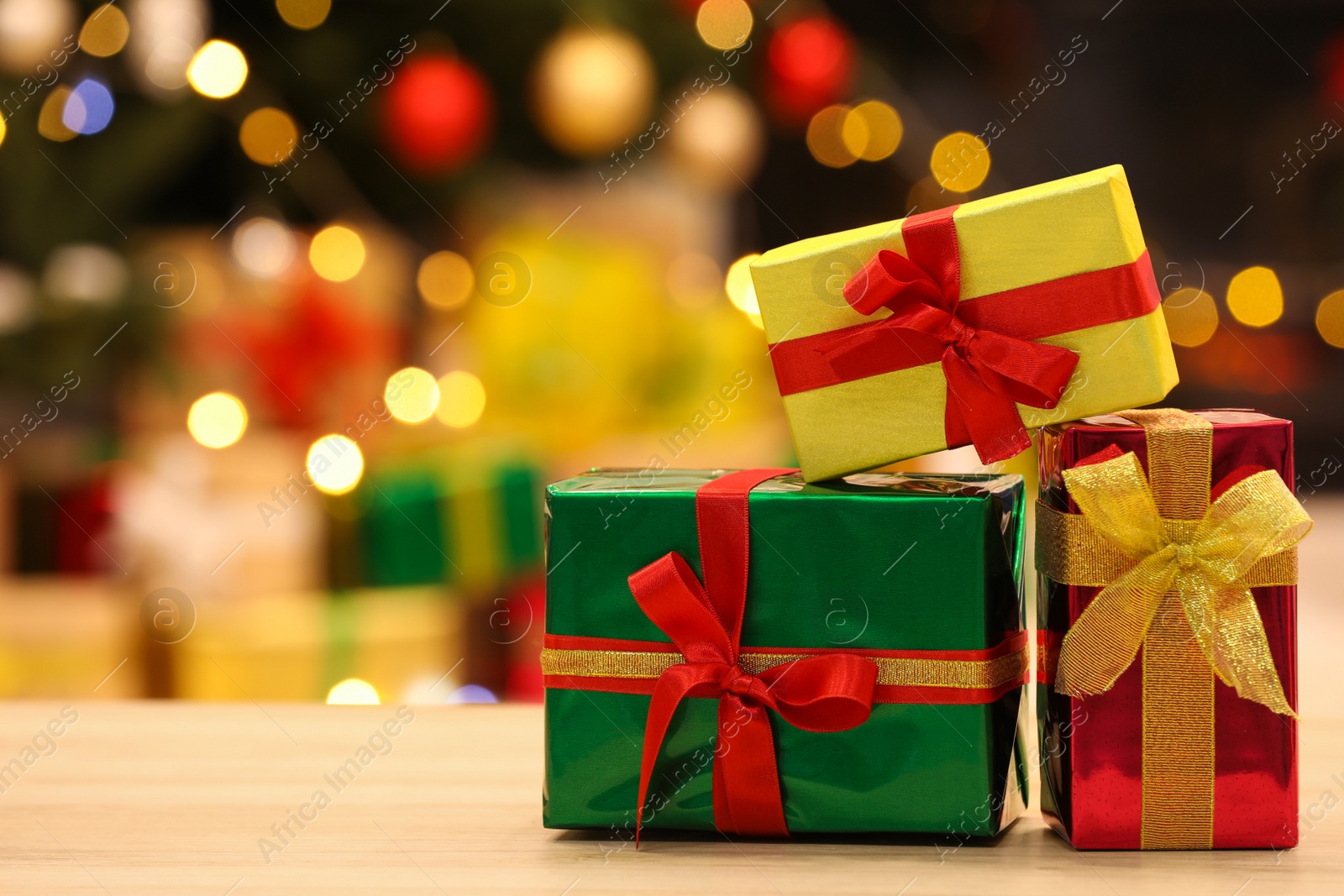 Photo of Beautifully wrapped gift boxes on wooden table against blurred festive lights, space for text. Christmas celebration