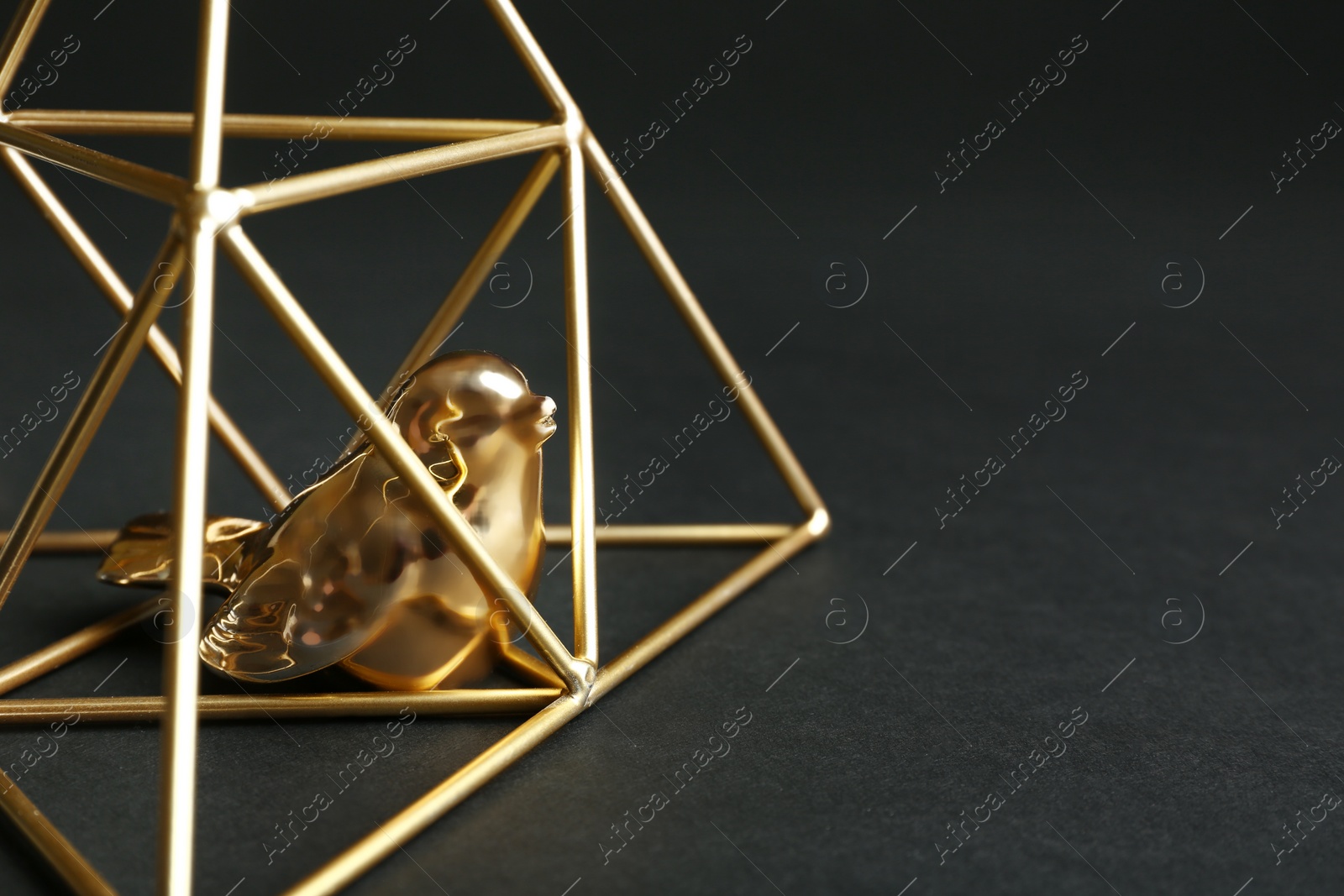 Photo of Decorative bird in gold pyramid on black background, closeup. Space for text