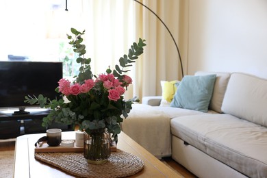 Photo of Beautiful bouquet of roses and eucalyptus branches in vase near candles on table at home. Space for text