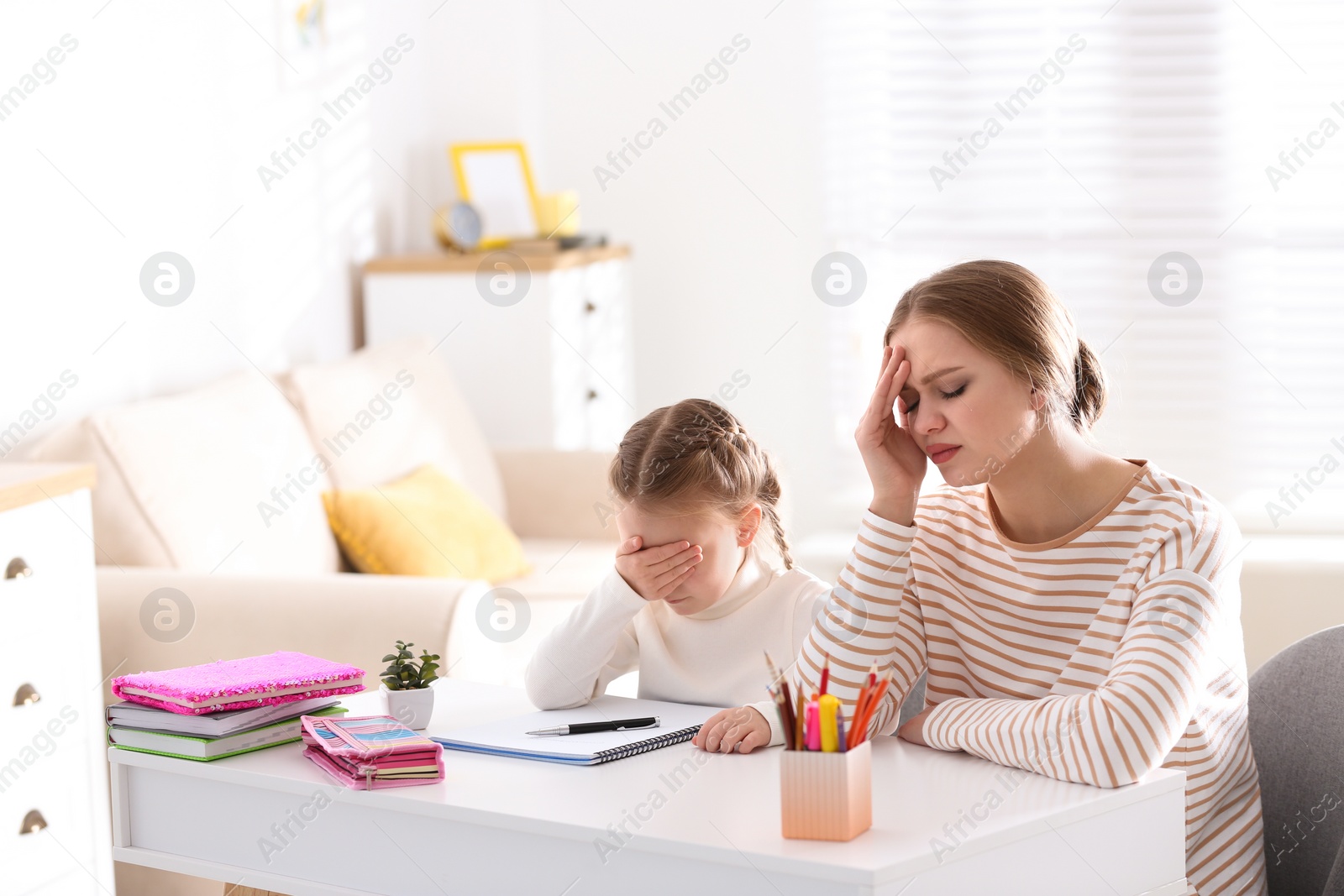 Photo of Upset mother and daughter doing homework together at table indoors