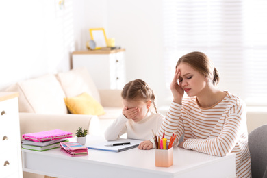 Photo of Upset mother and daughter doing homework together at table indoors