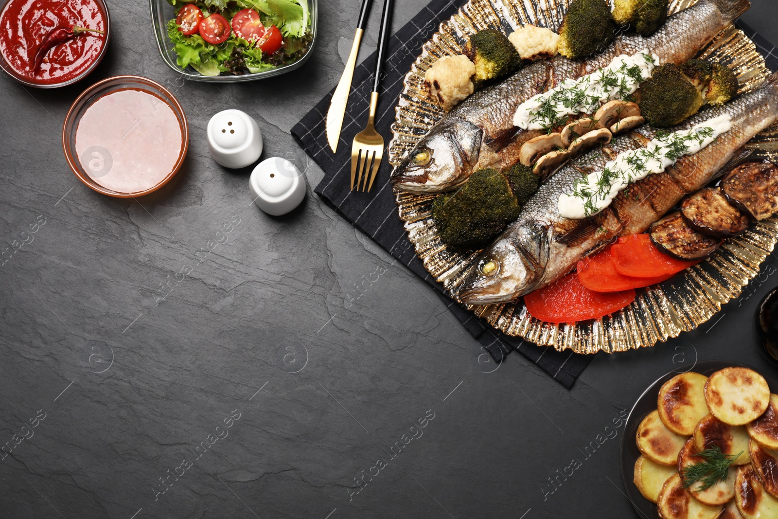 Photo of Flat lay composition with delicious sea bass fish, sauces and ingredients served on dark grey table. Space for text