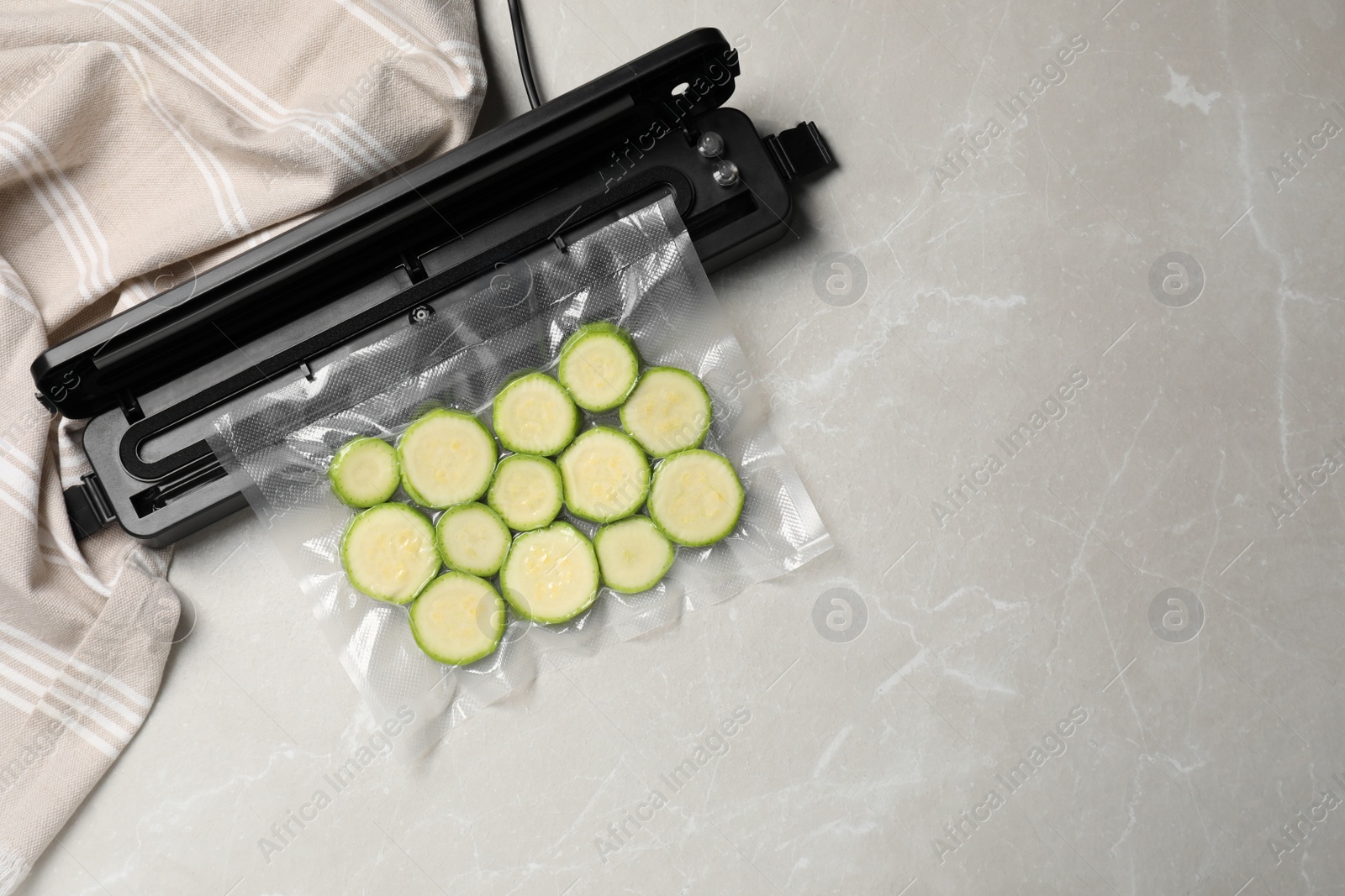 Photo of Sealer for vacuum packing and plastic bag with cut zucchini on light grey marble table, top view. Space for text