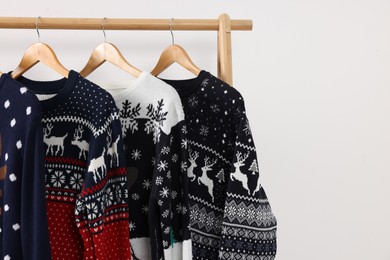 Rack with different Christmas sweaters on white background, space for text