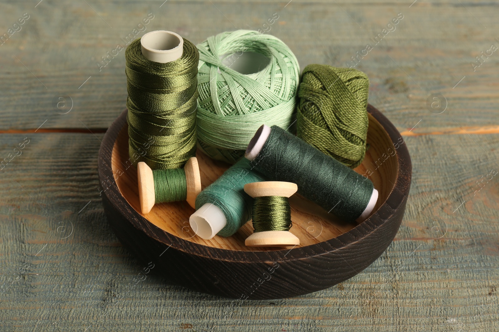 Photo of Color sewing threads in bowl on light blue wooden table