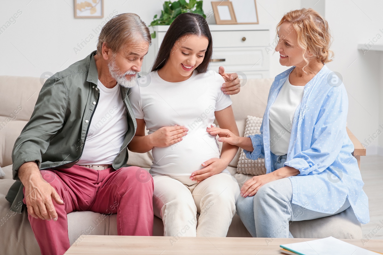 Photo of Happy pregnant woman spending time with her parents at home. Grandparents' reaction to future grandson