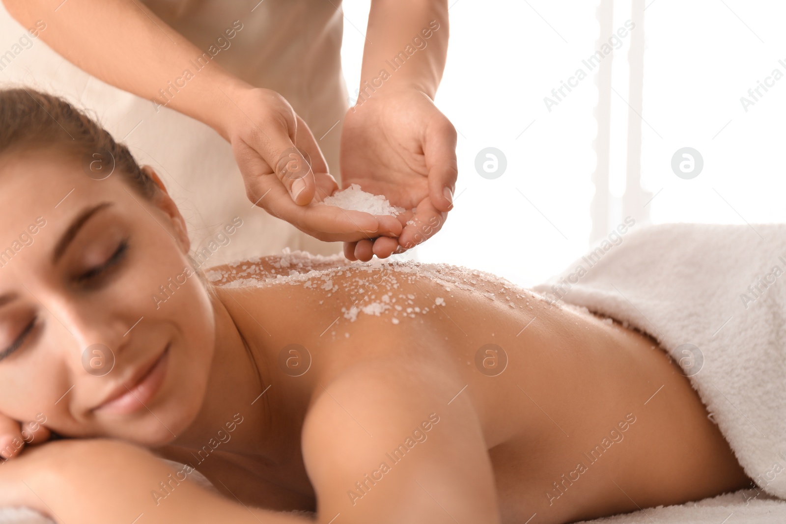 Photo of Young woman having body scrubbing procedure with sea salt in spa salon