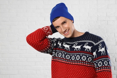 Photo of Portrait of young man in Christmas sweater and hat near white brick wall