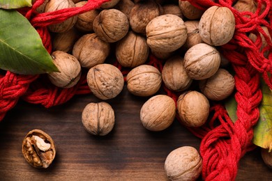 Photo of Net bag with walnuts and fresh leaves on wooden table, flat lay