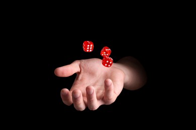 Man throwing red dice on black background, closeup