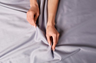 Photo of Woman touching soft silver fabric, top view