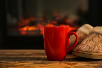 Red cup with hot drink against fireplace, space for text