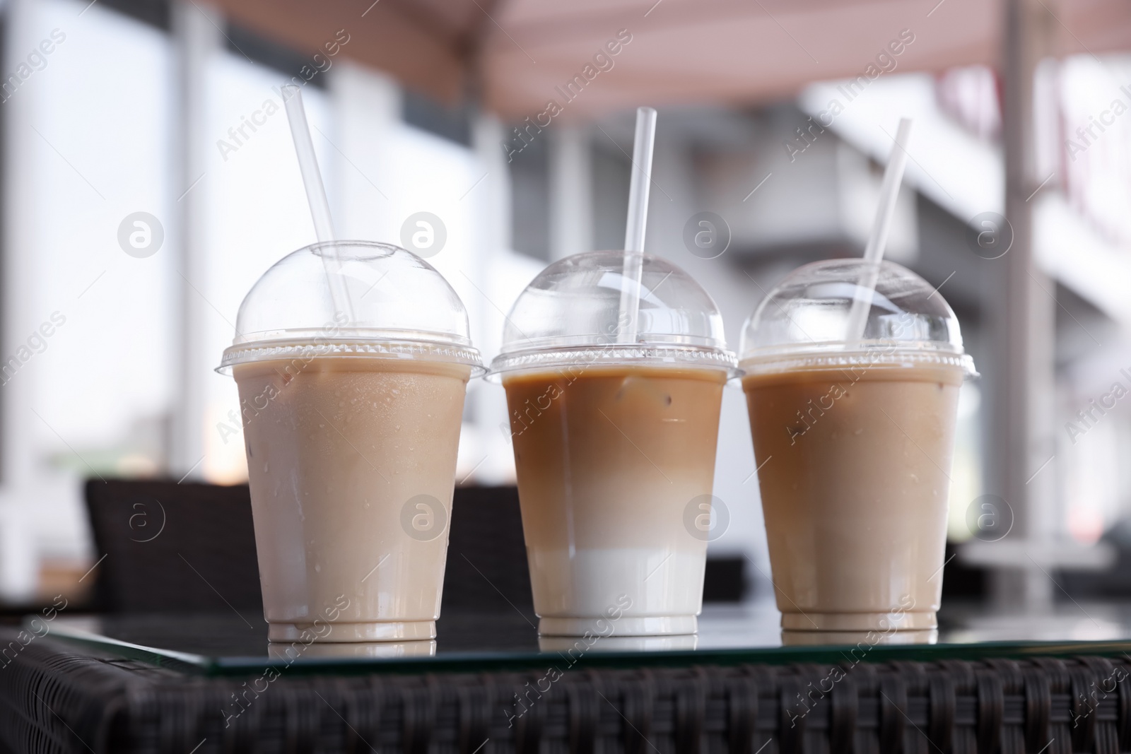 Photo of Plastic takeaway cups of delicious iced coffee on table in outdoor cafe