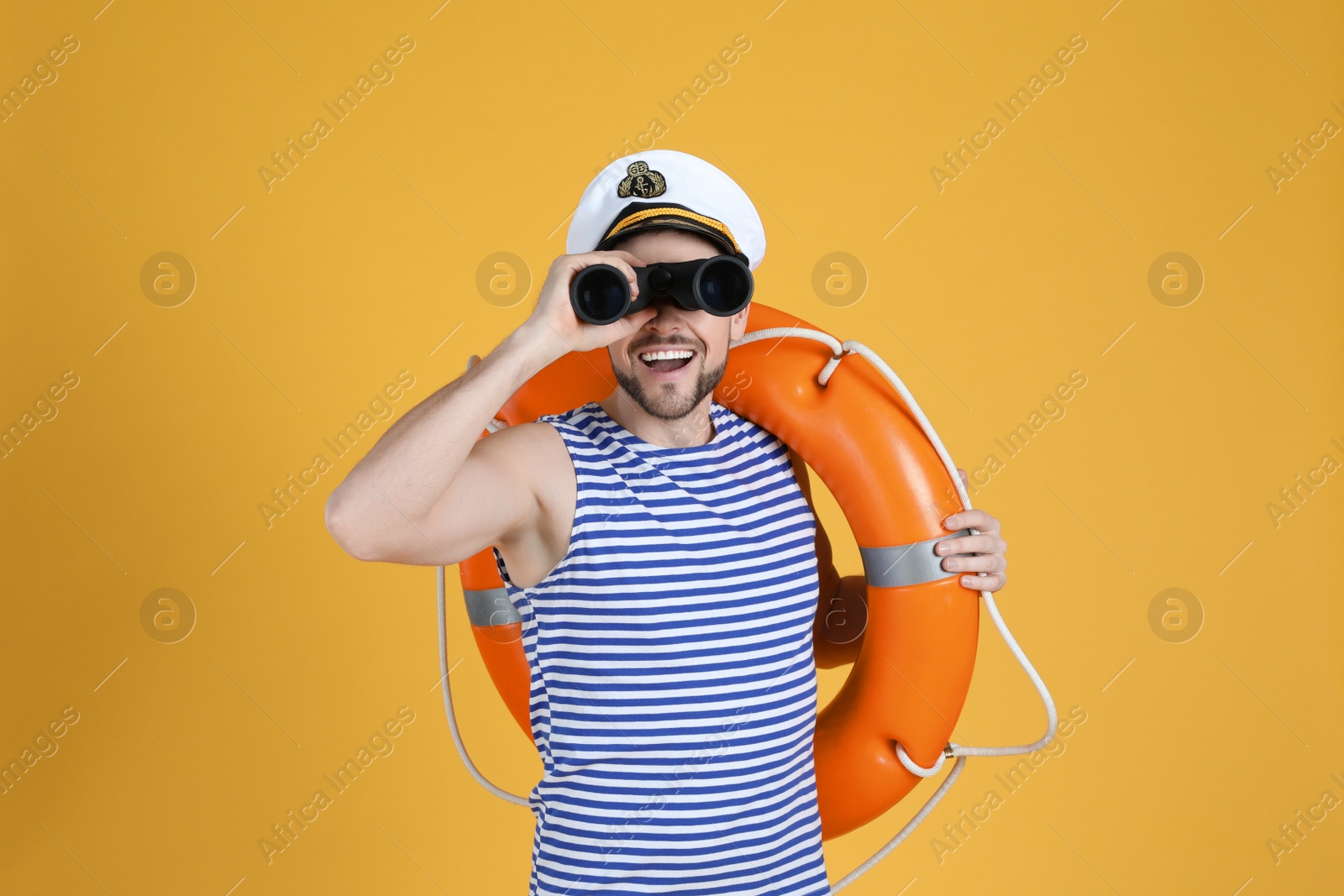 Photo of Sailor with orange ring buoy looking through binoculars on yellow background