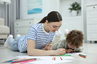 Photo of Mother and her little son drawing with colorful markers on floor at home
