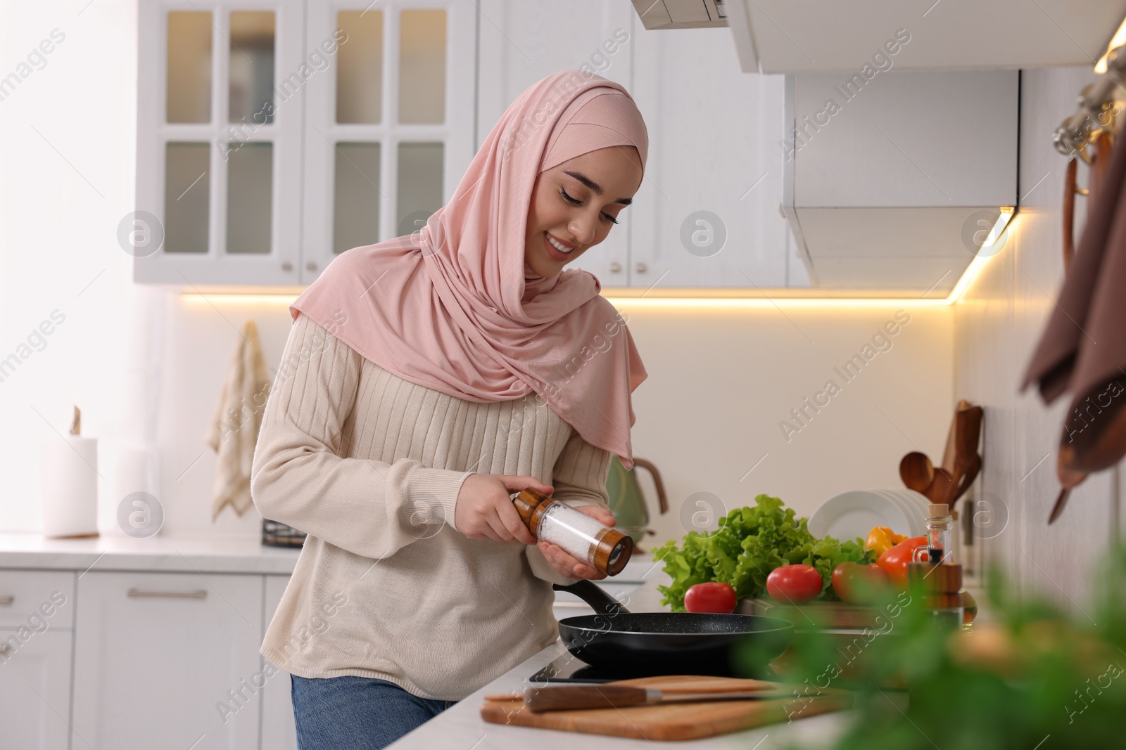 Photo of Muslim woman cooking delicious dish with vegetables on cooktop in kitchen