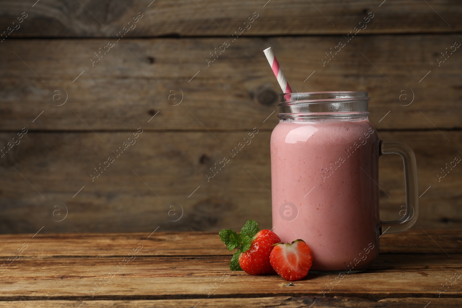 Photo of Mason jar with delicious strawberry smoothie and fresh berries on wooden table. Space for text