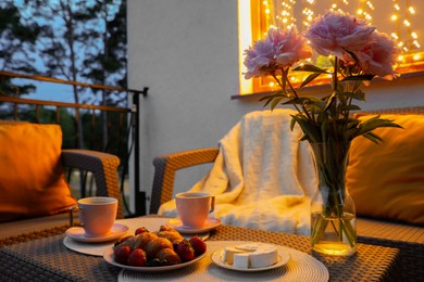 Photo of Rattan table with drink, food and flowers on outdoor terrace in evening