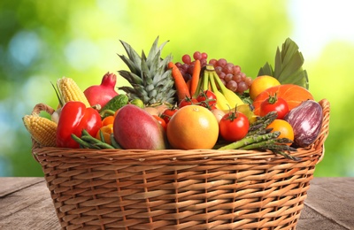 Fresh organic fruits and vegetables in wicker basket on wooden table, closeup
