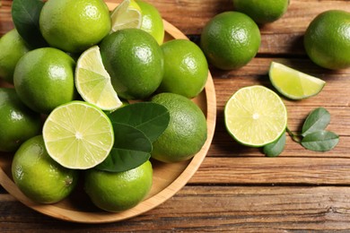 Photo of Fresh ripe limes and green leaves on wooden table, flat lay