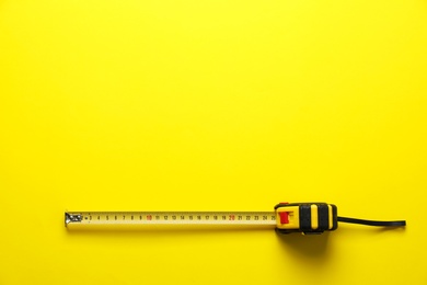 Tape measure on yellow background, top view. Space for text
