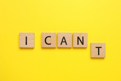 Photo of Motivation concept. Changing phrase from I Can't into I Can by removing square with letter T on yellow background, top view