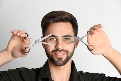 Photo of Young hairstylist holding professional scissors on light background