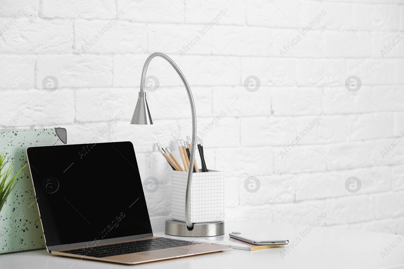Photo of Modern workplace with laptop on table against brick wall. Mockup for design