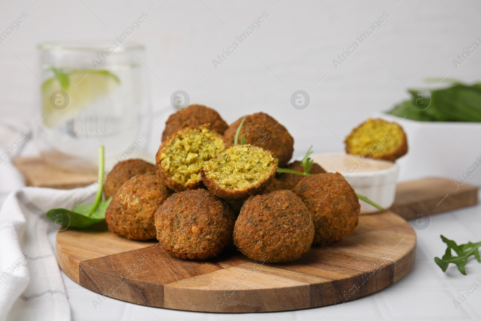 Photo of Delicious falafel balls, herbs and sauce on white tiled table