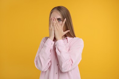 Embarrassed woman covering face with hands on orange background