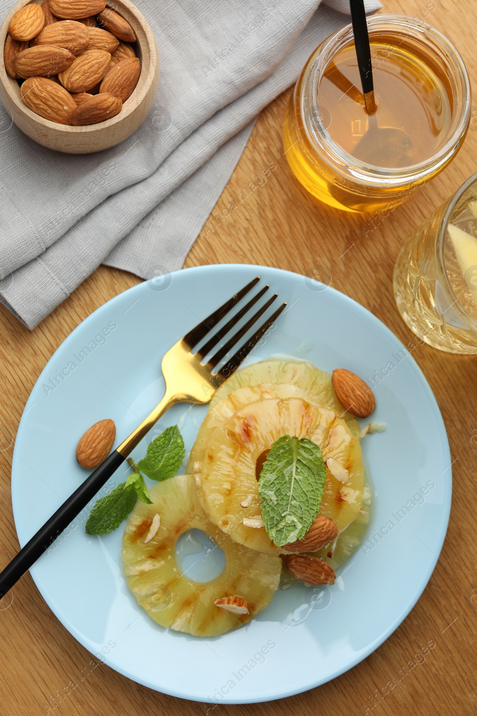 Photo of Tasty grilled pineapple slices served with mint and almonds on wooden table, flat lay