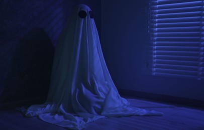 Photo of Creepy ghost. Woman covered with sheet near window in blue light, space for text