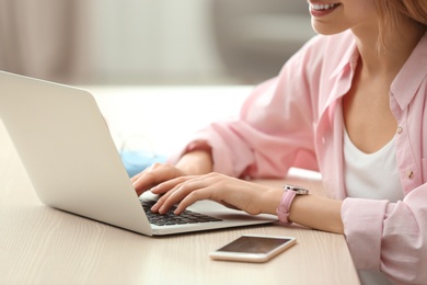 Photo of Young woman using laptop at table indoors, closeup
