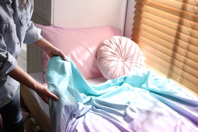 Woman making bed with new colorful linens in children's room, closeup