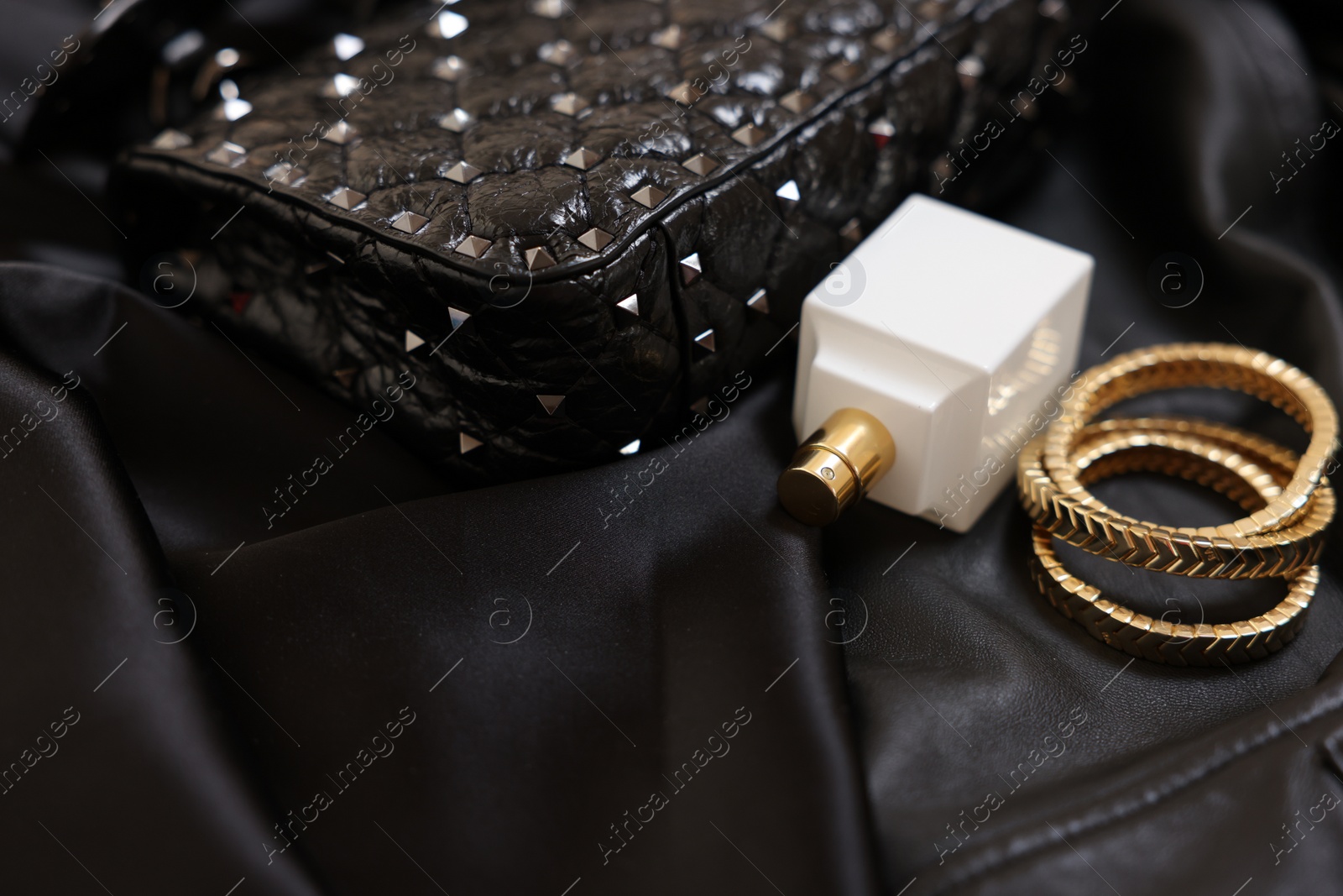 Photo of Leather bag, bottle of perfume and golden bracelets on black fabric, closeup. Space for text