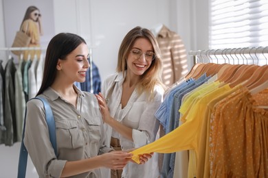 Photo of Young women choosing clothes near rack in modern boutique