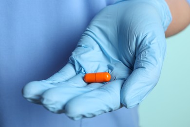 Photo of Doctor in medical glove holding pill on turquoise background, closeup