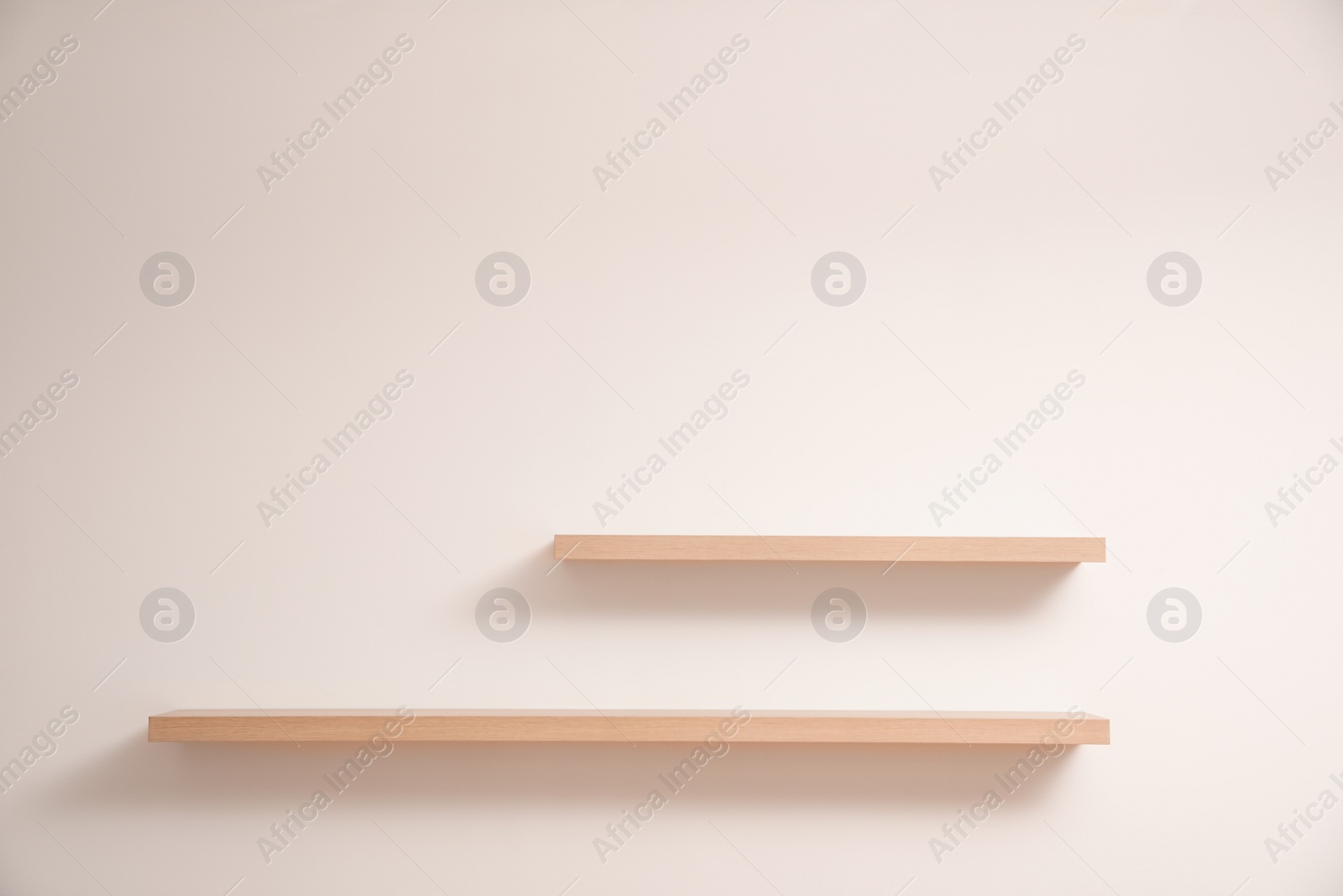 Photo of Empty stylish wooden shelves on light wall