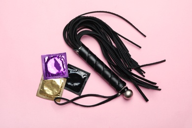 Photo of Whip and condoms on pink background, top view. Sex game