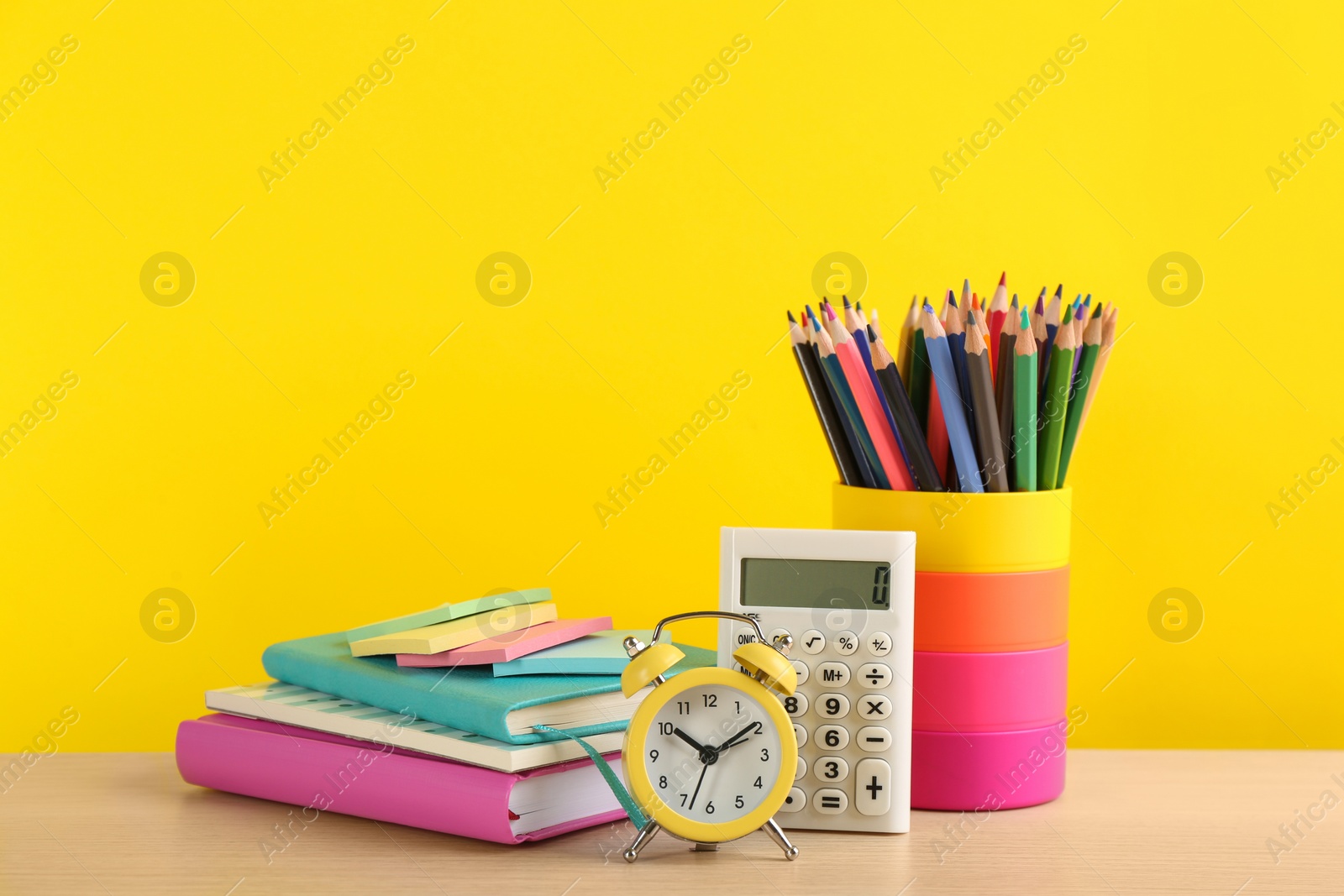 Photo of Different school stationery and alarm clock on table against yellow background, space for text. Back to school