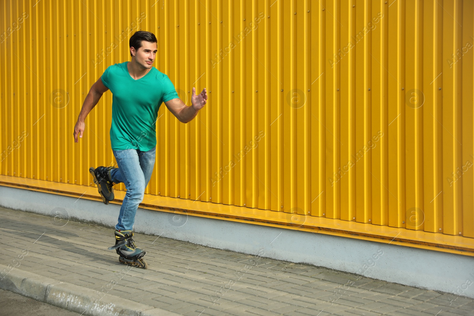 Photo of Handsome young man roller skating near yellow building, space for text