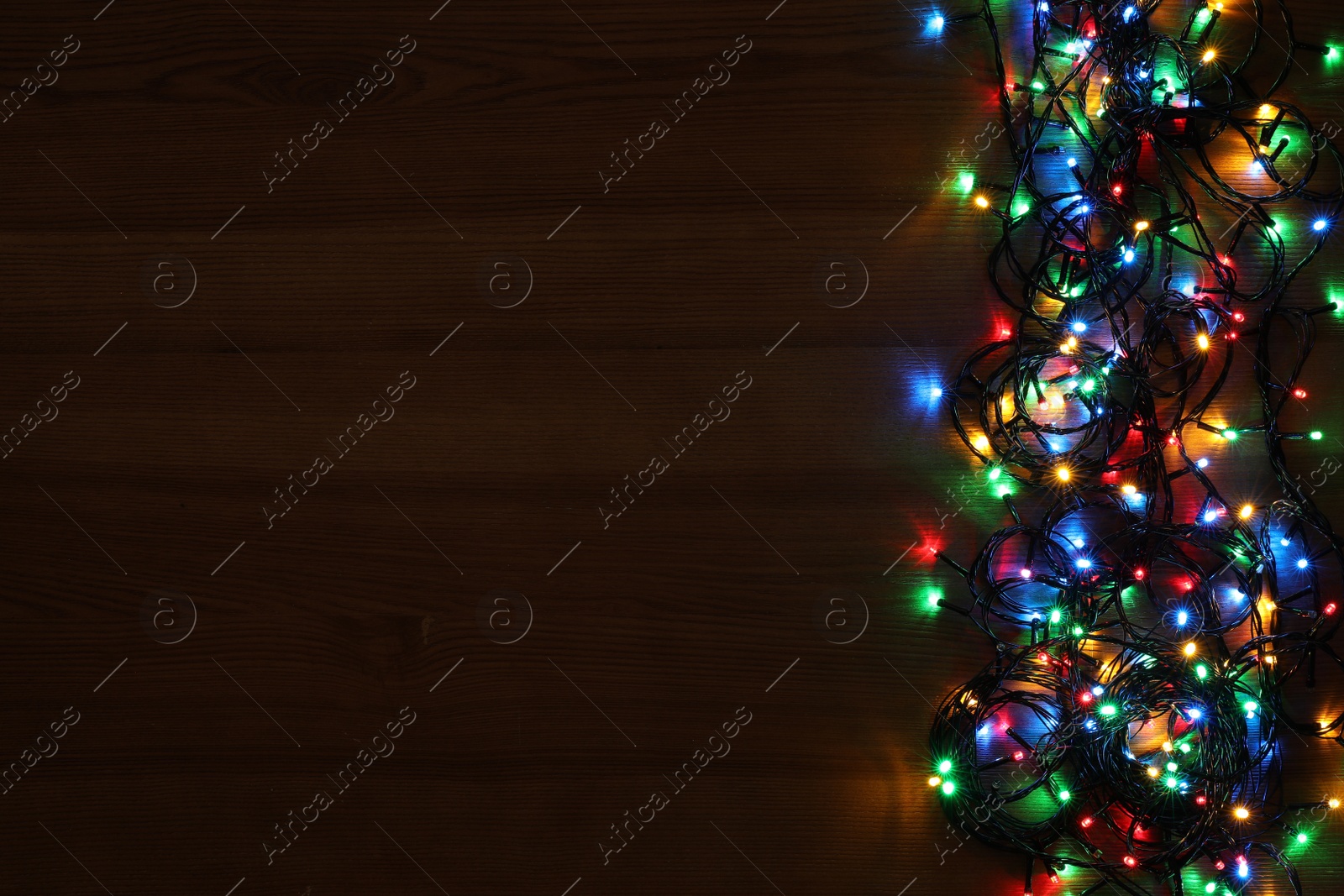 Photo of Colorful Christmas lights on wooden table, top view. Space for text