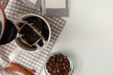 Photo of Pouring hot water into cup with drip coffee bag on white table, flat lay. Space for text