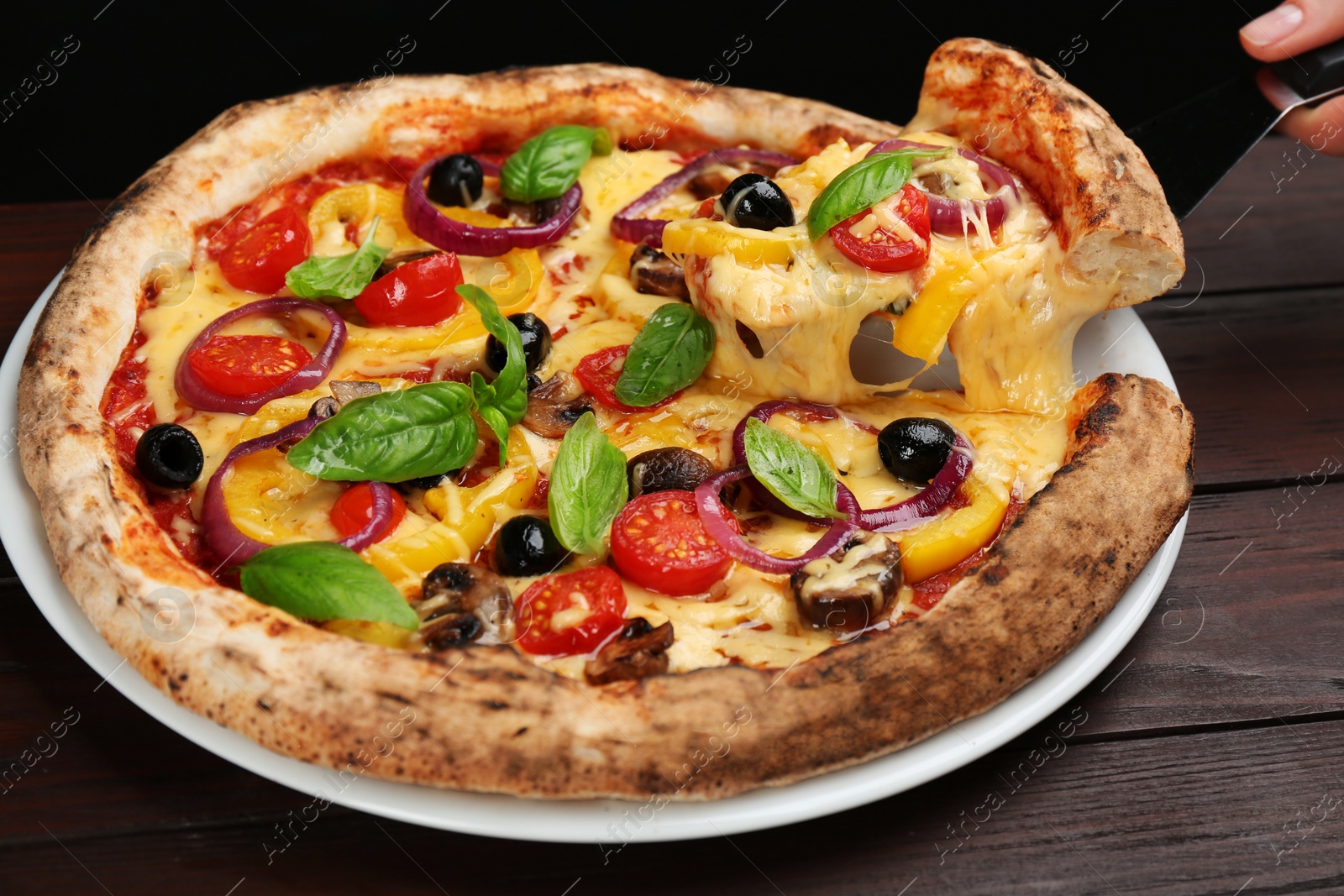 Photo of Woman taking slice of tasty vegetable pizza at wooden table, closeup