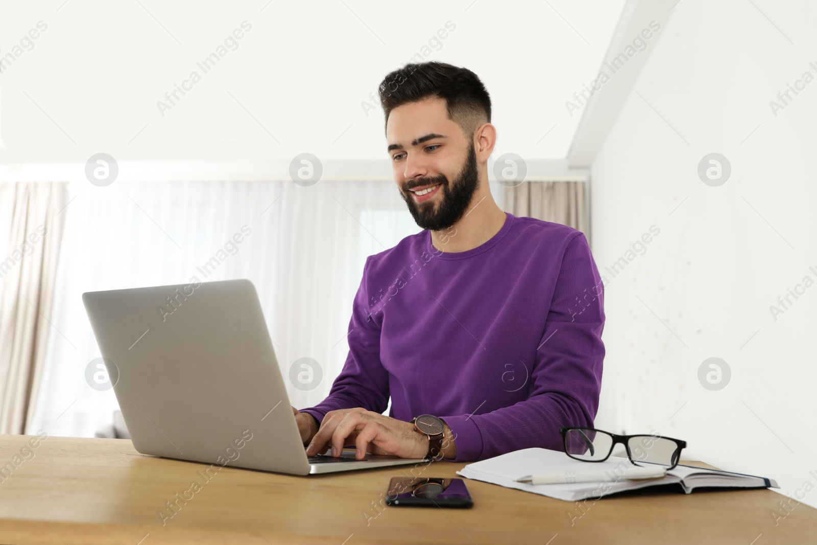 Photo of Handsome young man working with laptop at table in home office